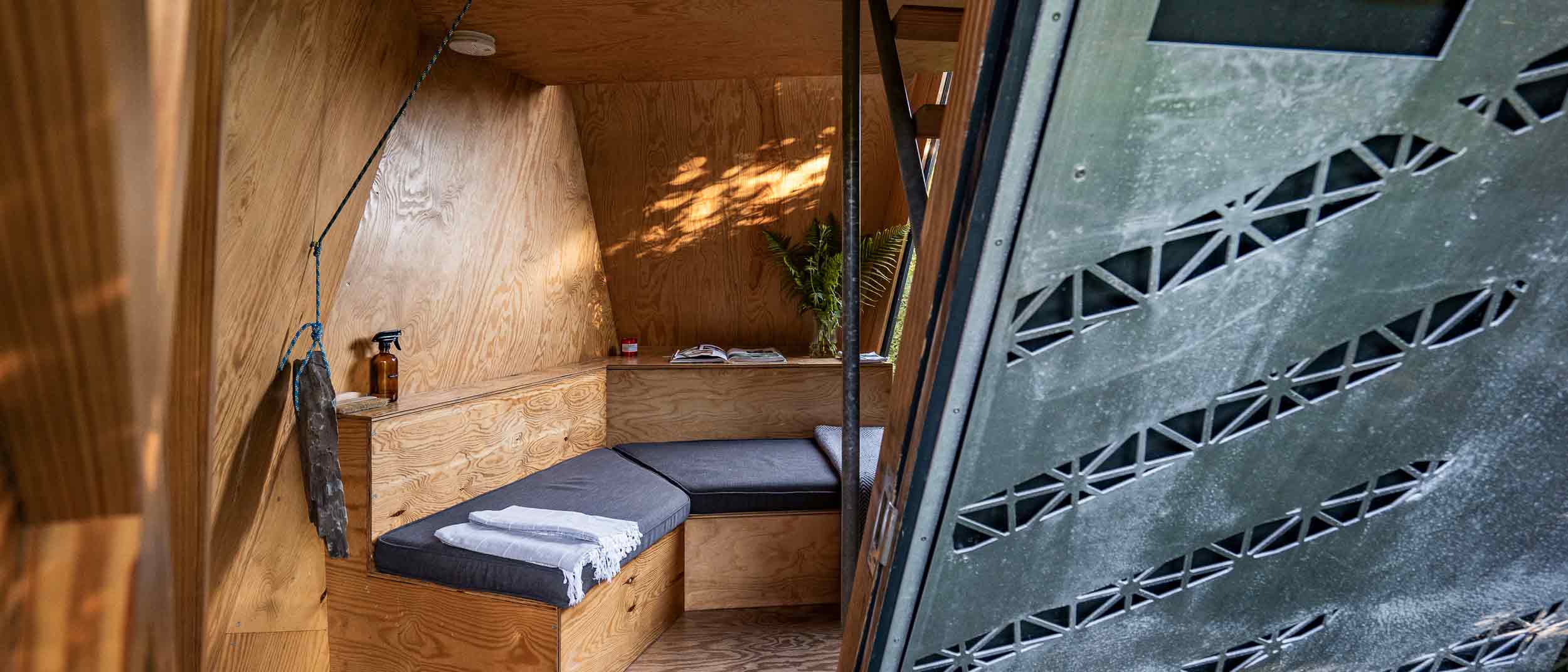 interior of an off grid Kudhva cabin, with a sofa and blankets in dappled sunlight
