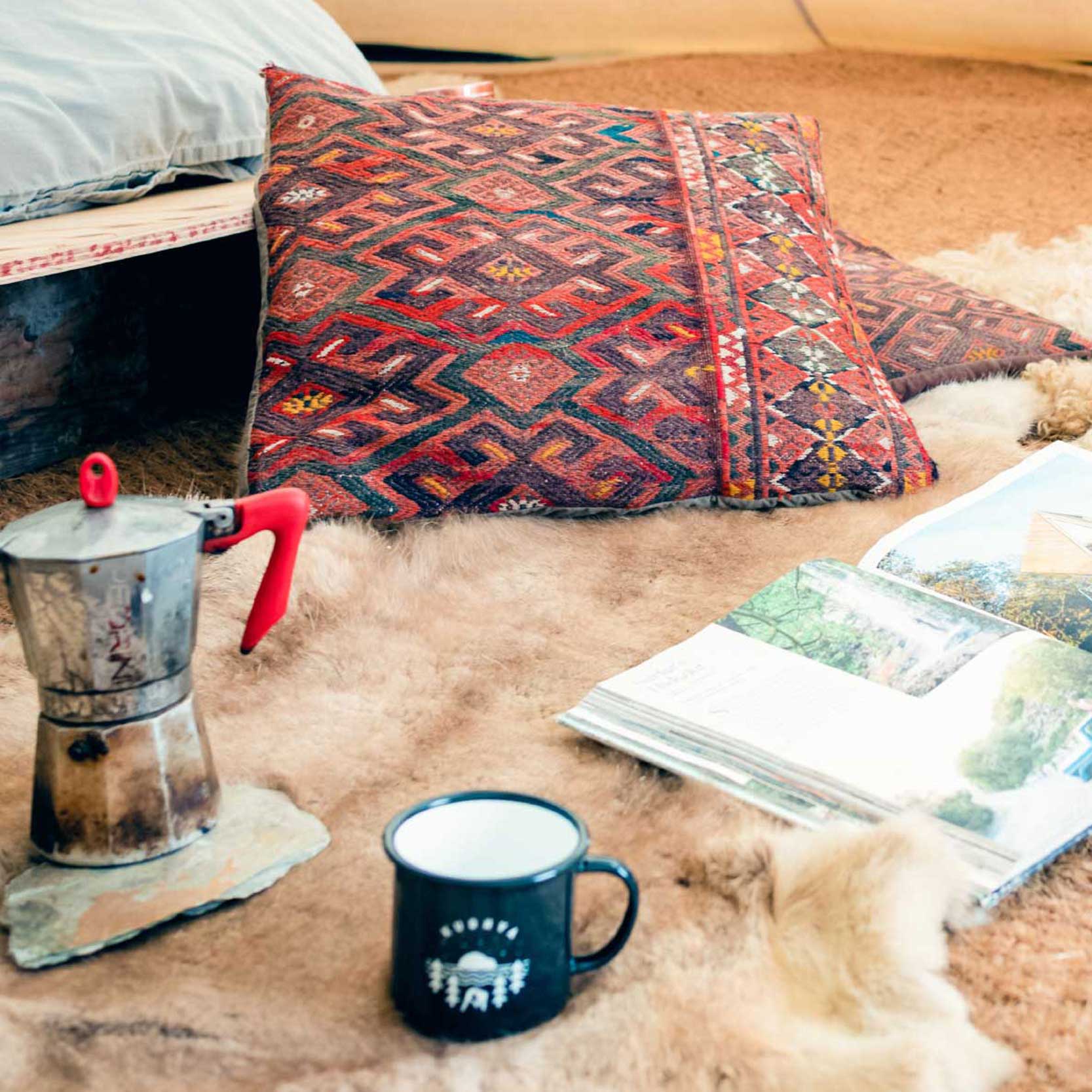 mug, cushion and book on a rug in a tipi at Kudhva, Cornwall