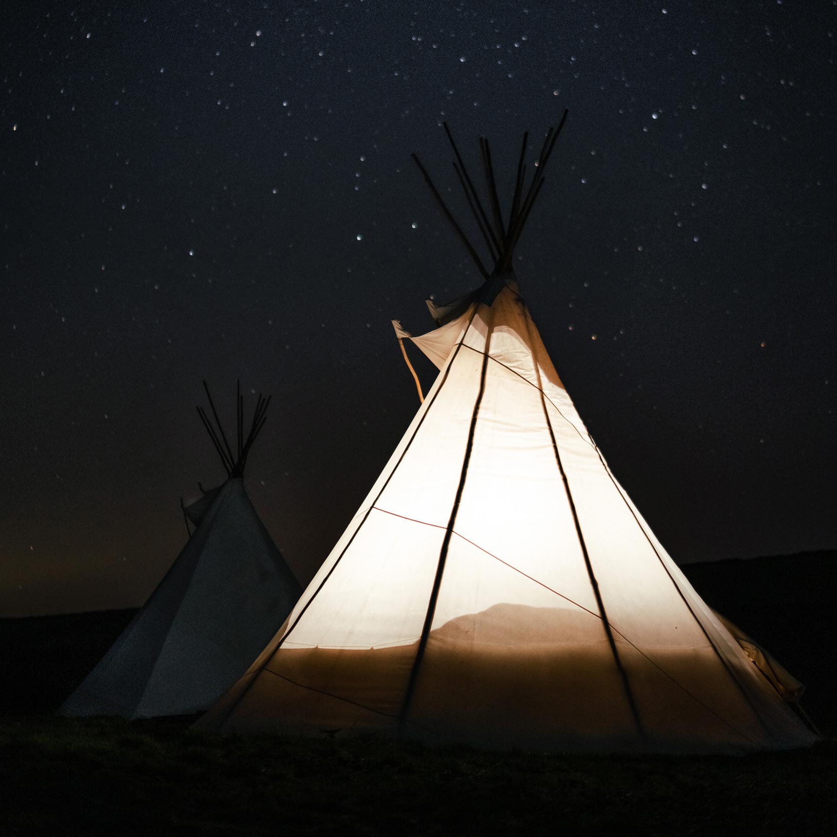 a tipi glowing from the inside against a clear, starry night at Kudhva, Tintagel