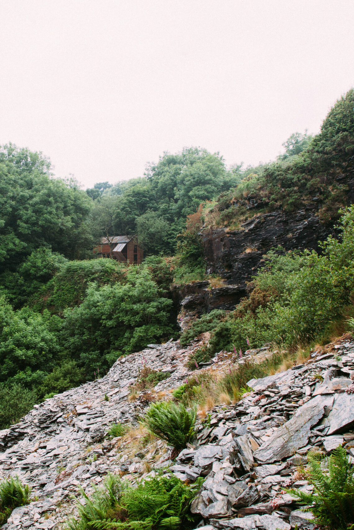 distant view of the Danish Cabin, nestled amongst trees and surrounded by slate from Kudhva's quarry history