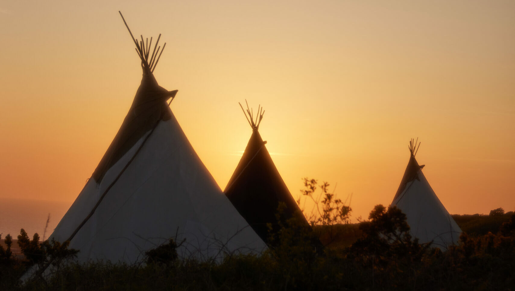 three tipis at Kudhva campsite against a sunset background